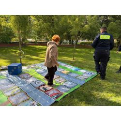 Seniorka stojąca na planszy do gier, obok idący strażnik